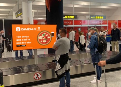 Pantalla digital con publicidad junto a una cinta de equipajes del aeropuerto de Sevilla