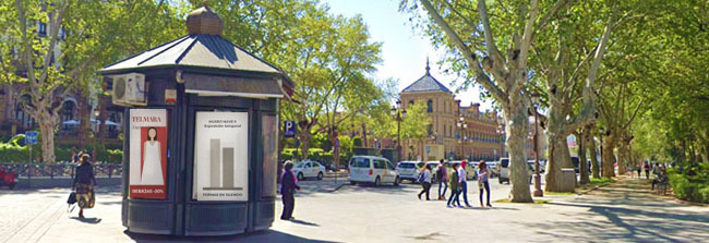Kiosco con publicidad y gente en una avenida de Sevilla